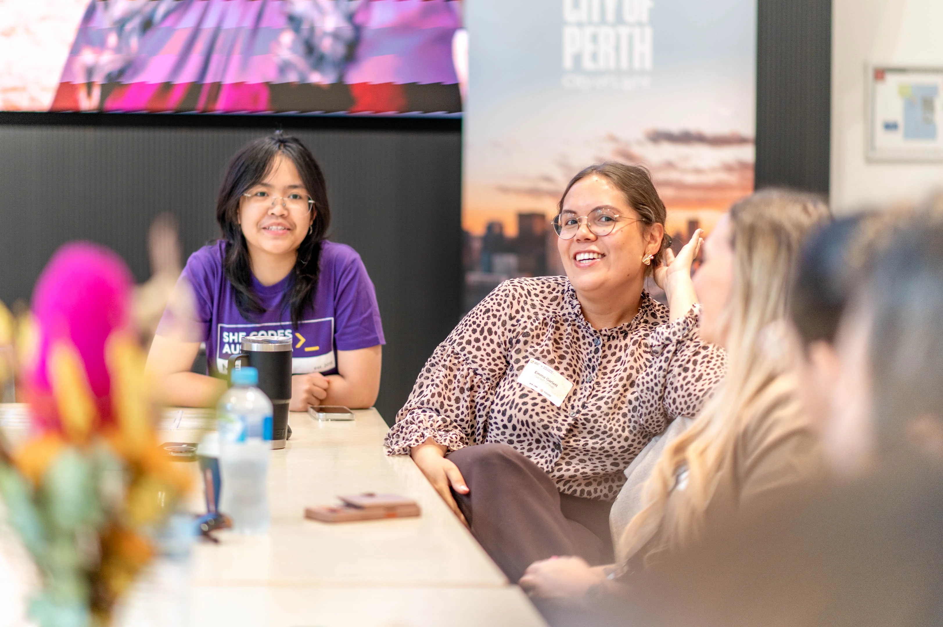 Emma Garlett at a She Codes x Garlett Group collaboration event. She is sitting with attendees, smiling