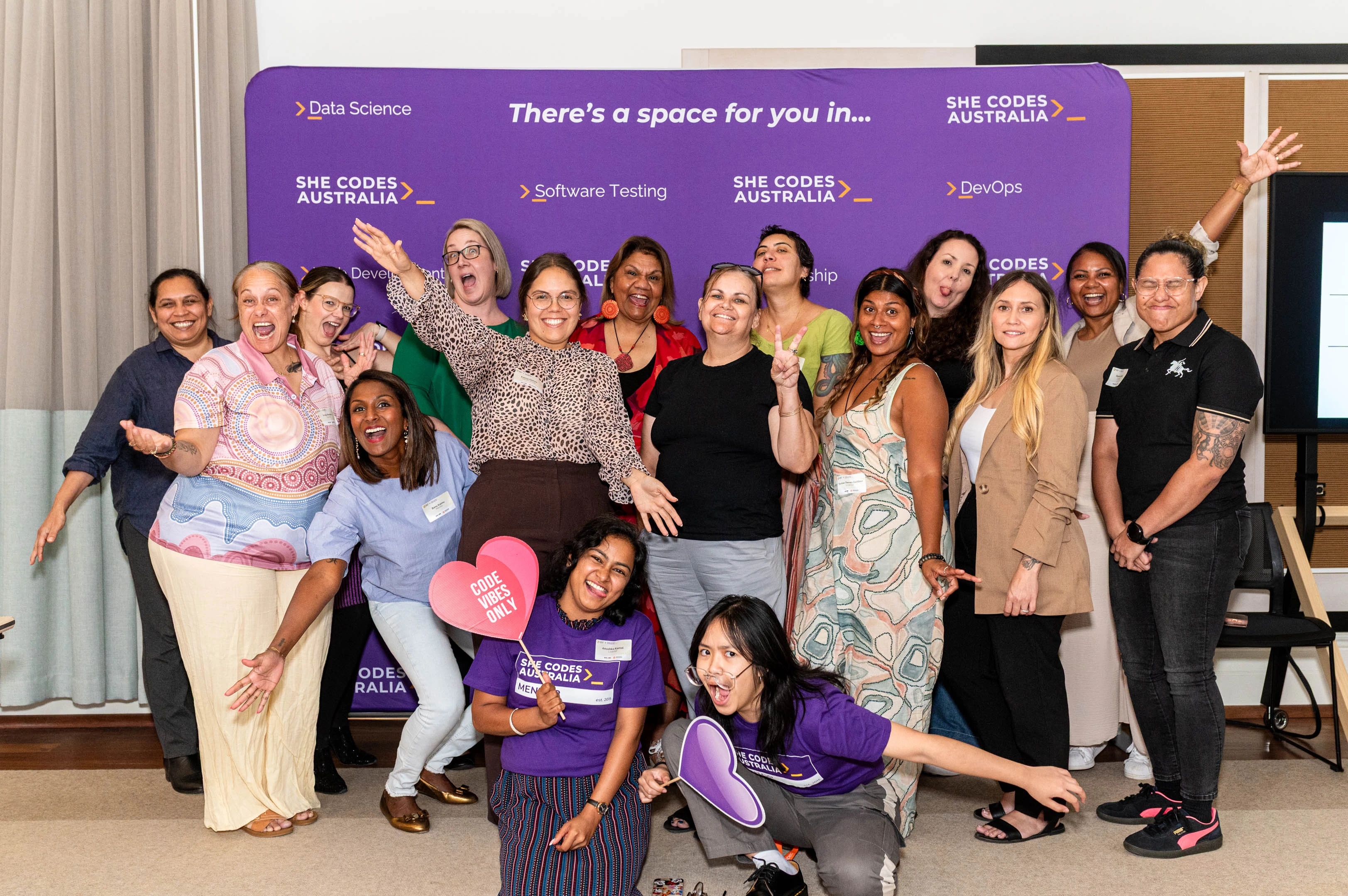 Group photo from the conclusion of our First Nations event - a dozen women stand in front of a media wall smiling and making silly faces