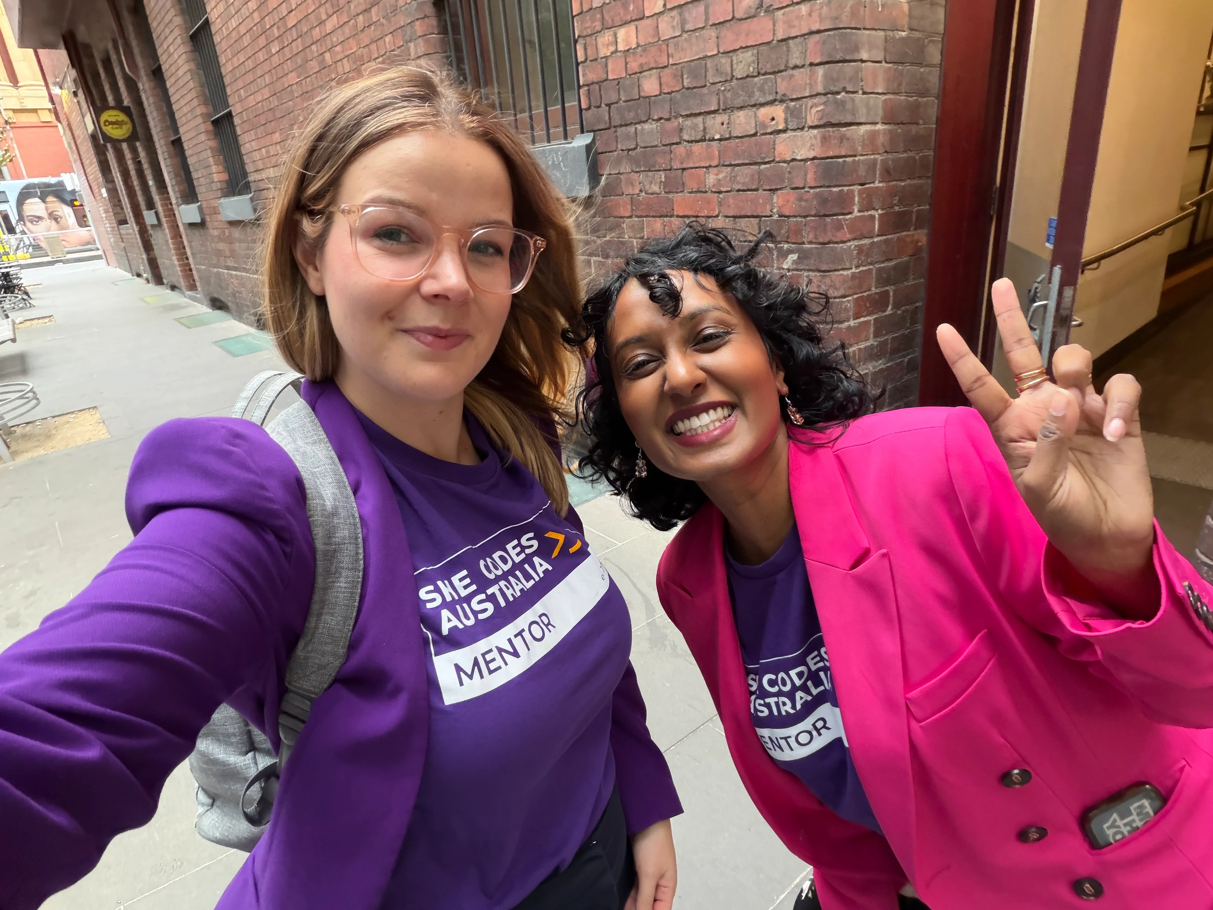 Kate in a purple She Codes shirt and blazer hugs Shaz wearing hot pink outside a Melbourne event