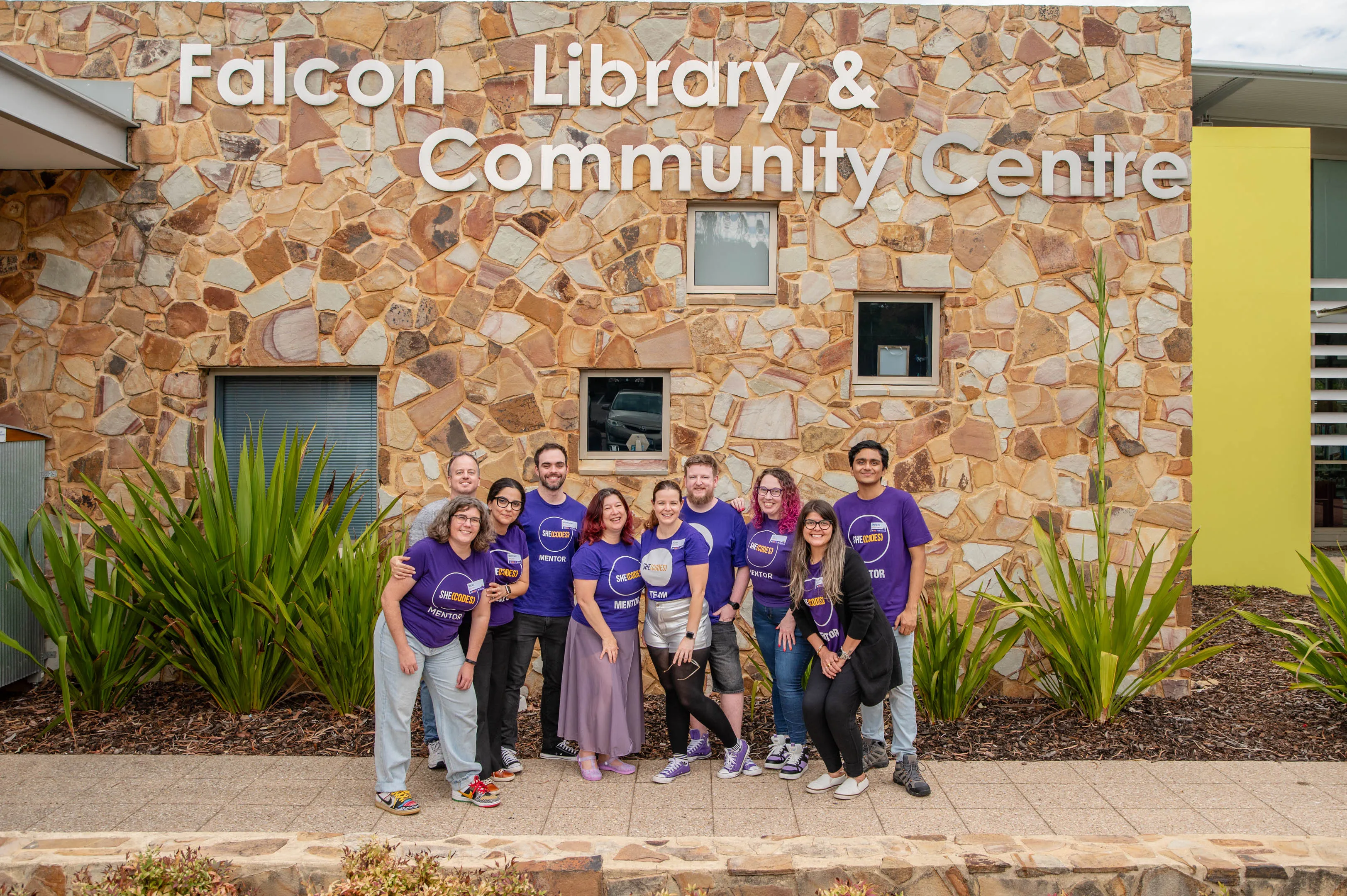 A group of She Codes mentors smiling together under the sign for Falcon library