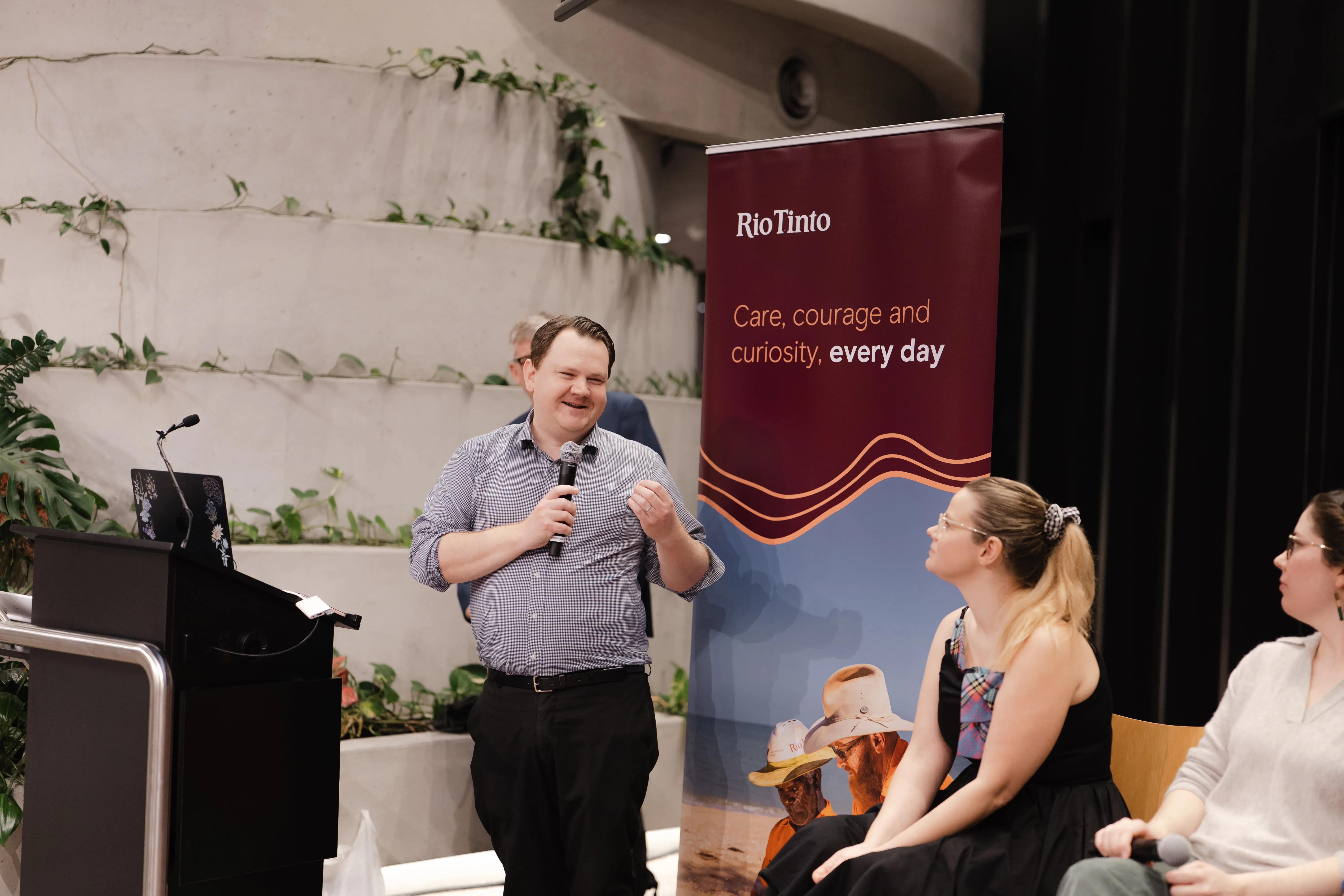 Dan Evans of Rio Tinto talks into a microphone with a Rio banner behind him.
