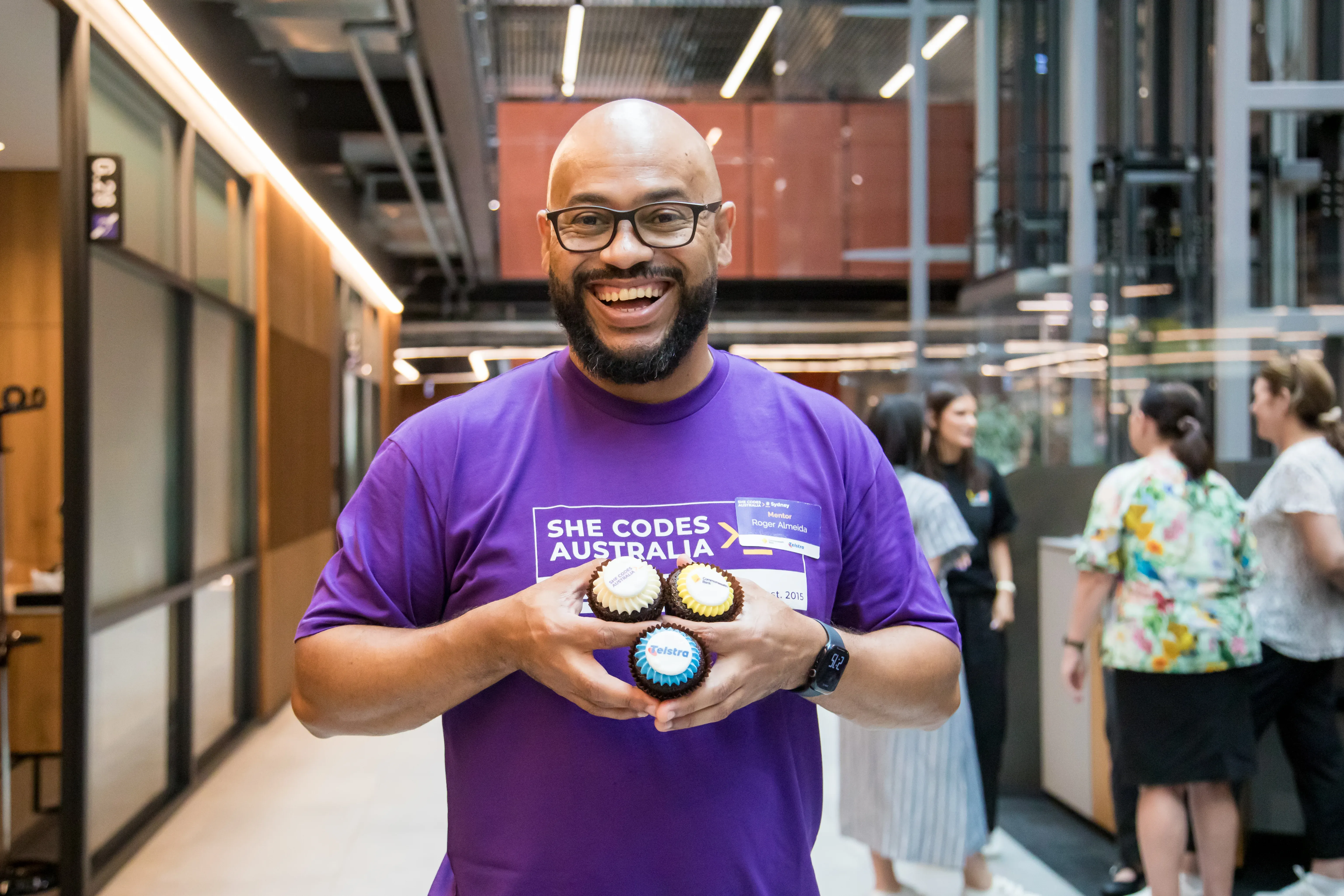 A She Codes mentor holding three cupcakes with the She Codes, CommBank and Telstra logos on them