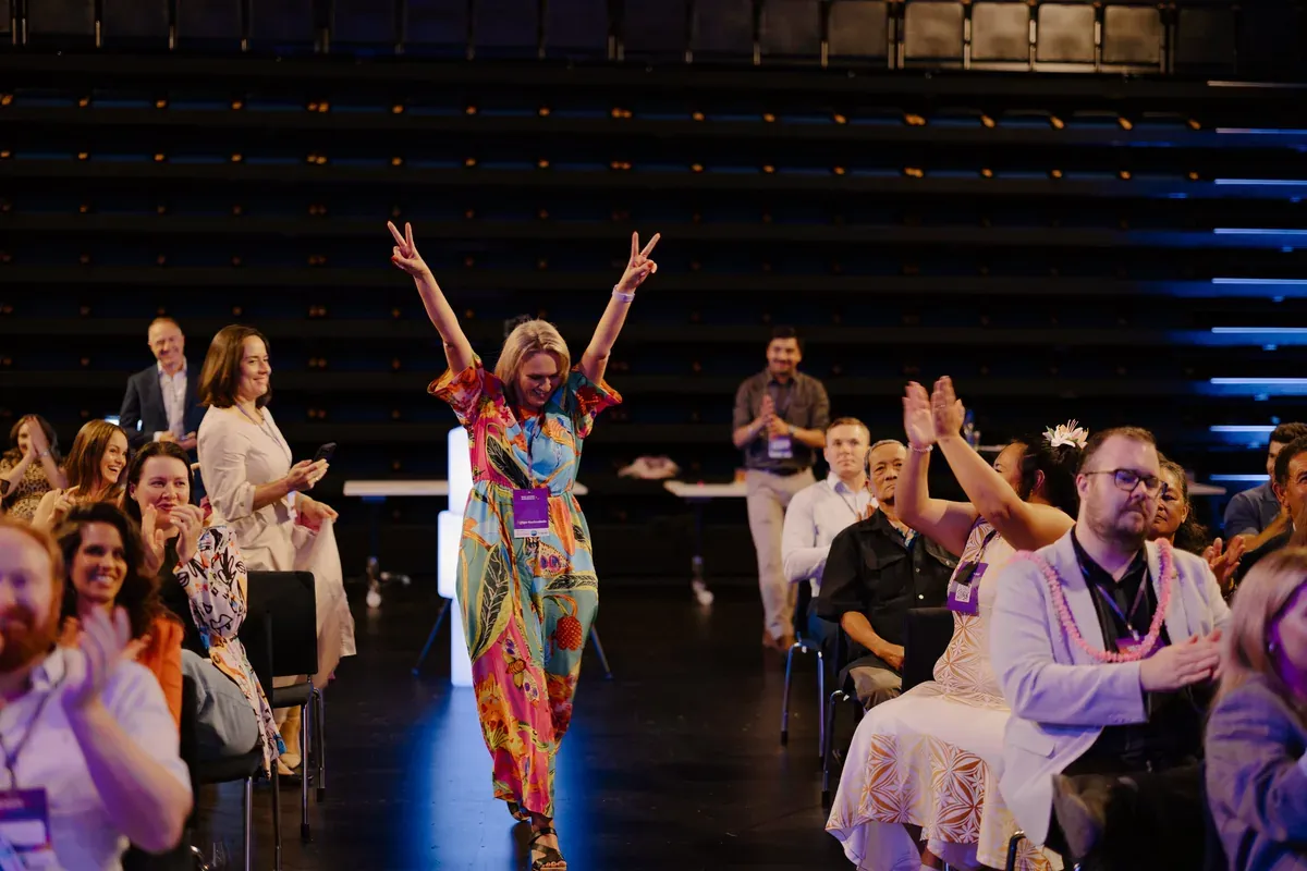 An attendee celebrating on stage with arms raised to cheering applause