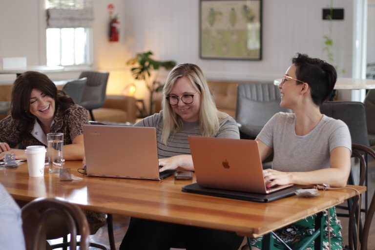 3 women sitting at a desk working on laptops